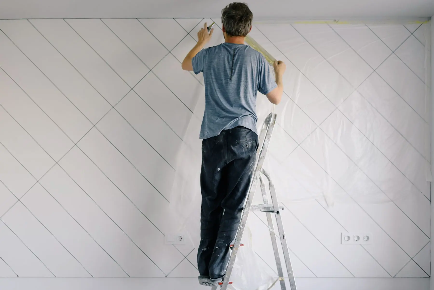 Schilder op een trap zet een muur binnen in de grondverf